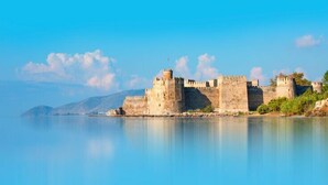 A historic stone castle by a calm sea with clear skies.