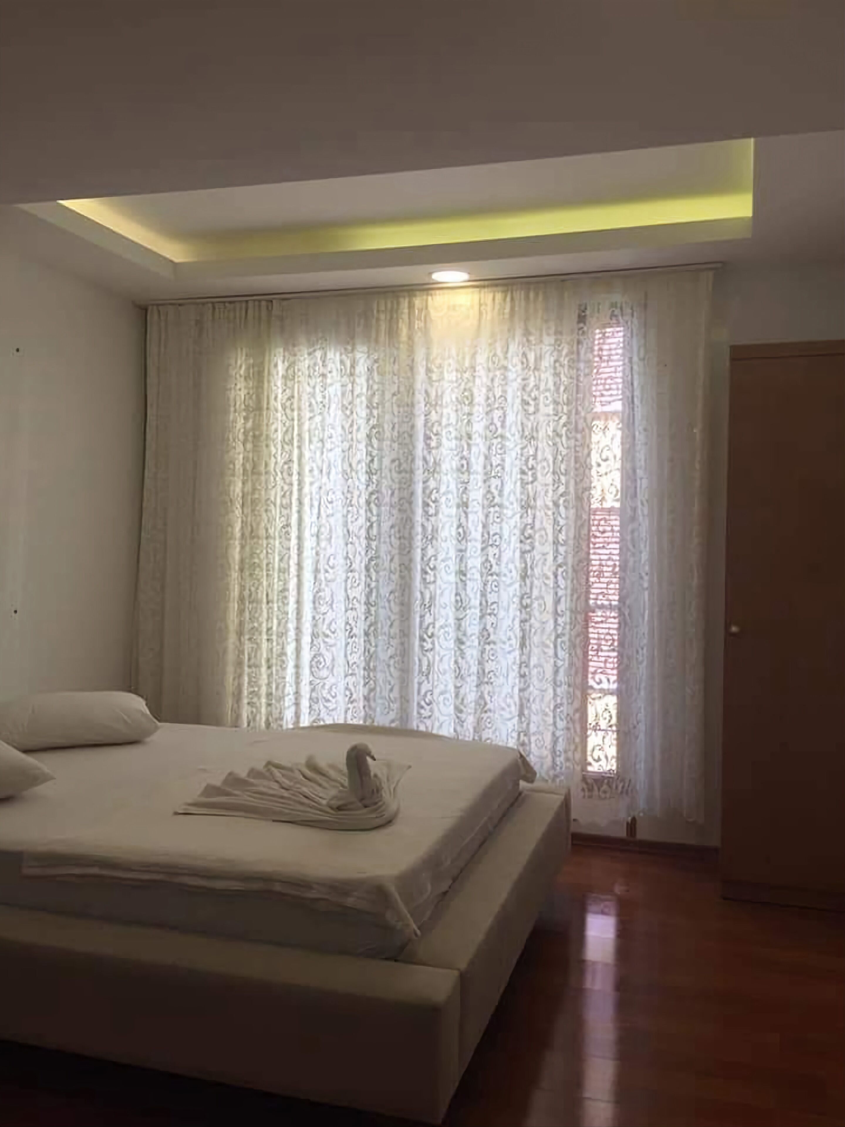 Un dormitorio con una cama grande, una lámpara de techo y una ventana con cortinas estampadas.