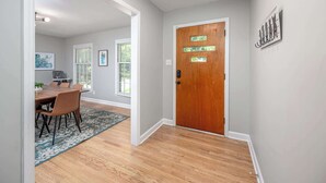 A hallway with a wooden door, a dining area with a table and chairs, and a rug. - Pet-Friendly 3BR 2BA - Fenced Yard (Durham)