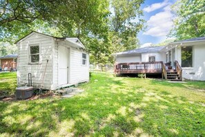 A small white mobile home with a porch and a small shed in a grassy yard.