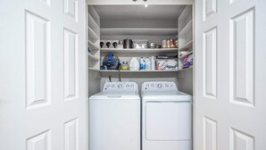 A laundry room with two front-loading washing machines and shelves above containing various cleaning supplies. - Pet-Friendly 3BR 2BA - Fenced Yard (Durham)