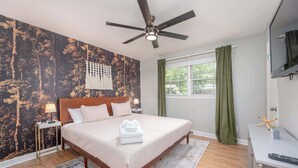 A bedroom with a bed, a ceiling fan, a window with curtains, a TV, and a desk with a keyboard. - Pet-Friendly 3BR 2BA - Fenced Yard (Durham)