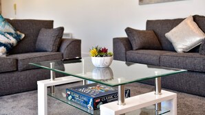 A living room with two grey sofas, a glass coffee table, and a bowl of flowers. There are two board games on the table. - Just Stay Wales - Meridian Tower (Swansea)