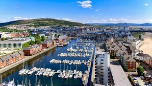 A marina with numerous boats docked, surrounded by residential buildings and a clear view of the cityscape in the background. - Just Stay Wales - Meridian Tower (Swansea)