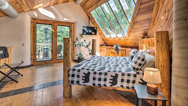 Una camera accogliente con soffitto spiovente, un letto con coperta a quadri, un comodino con lampada e una TV montata a parete.