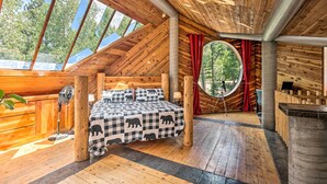 Accogliente baita di legno con un letto, una ventola e una finestra circolare vista foresta.