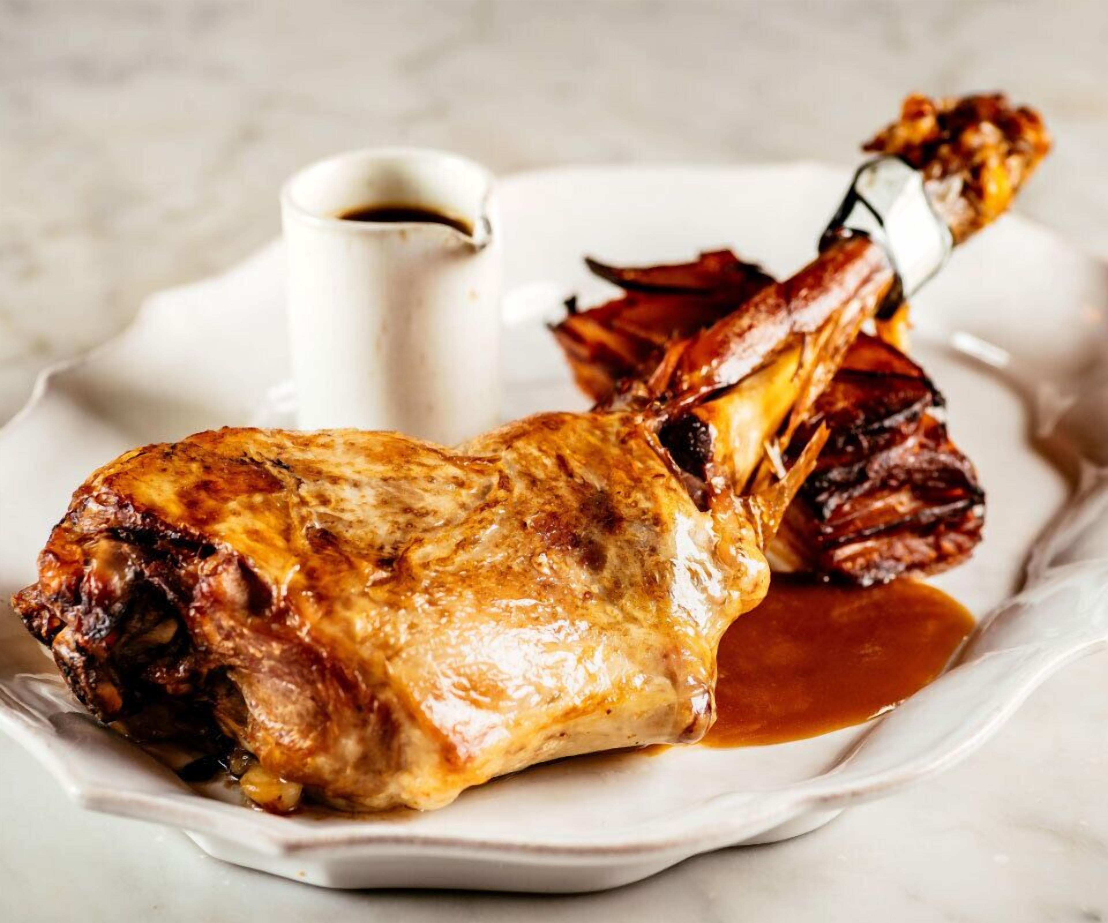 A roasted leg of lamb with gravy on a white plate.