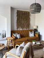 A living room with a brown sofa, wooden chairs, a small table, and a hanging light fixture.