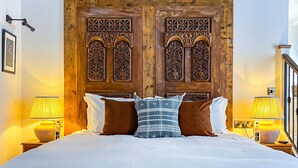 A bedroom with a large bed, wooden headboard, two nightstands with lamps, and a small wooden table in front of the bed. - Parador44 (Cardiff)
