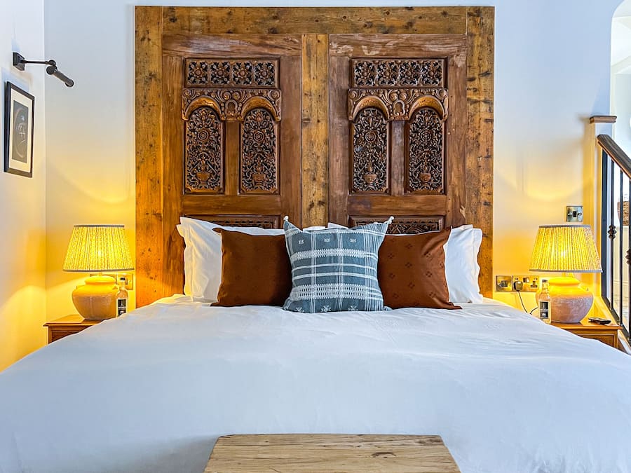 Een slaapkamer met een groot bed, een houten hoofdeinde, twee nachtkastjes met lampen en een klein houten tafeltje voor het bed.