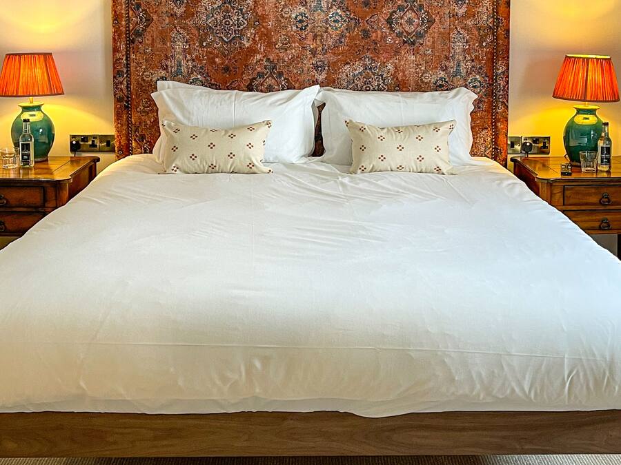 Un grand lit avec du linge de lit blanc, deux tables de chevet avec des lampes et une tête de lit à motifs.