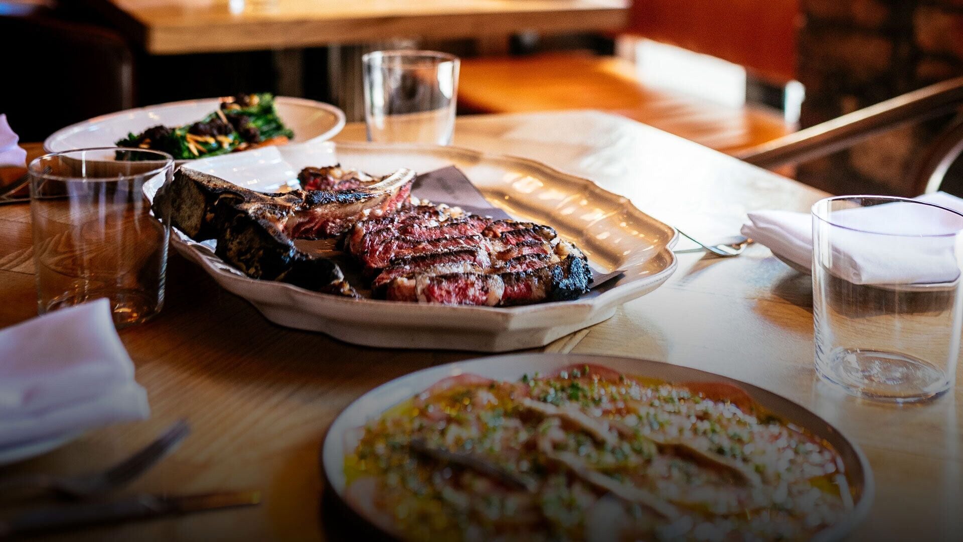 Une table à manger avec une assiette de steak, un verre d’eau et un verre de bière.