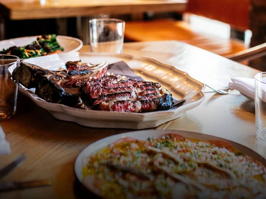 Una mesa de comedor con un plato de carne, un vaso de agua y un vaso de cerveza.