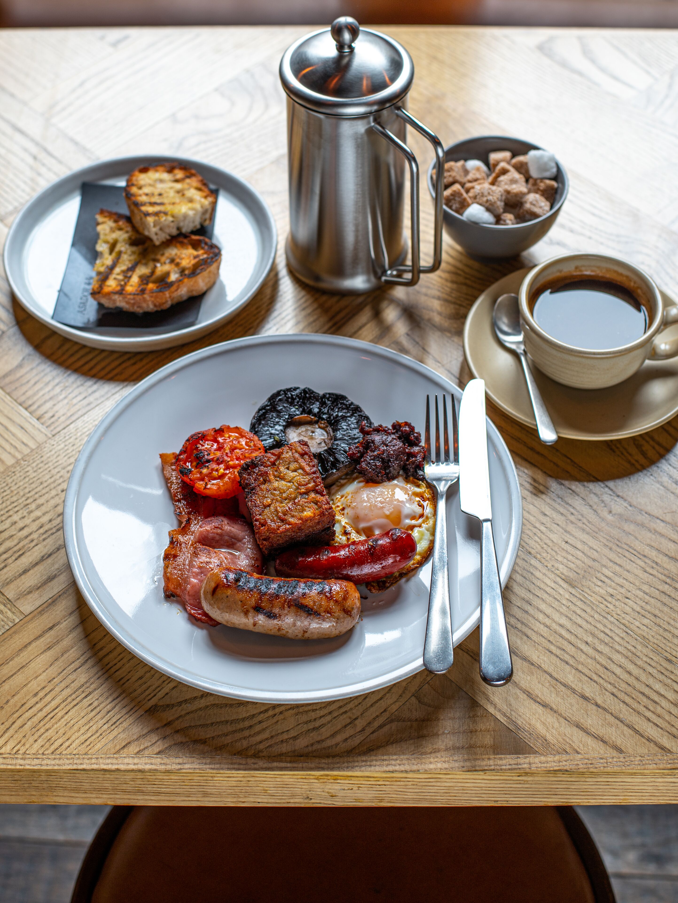 A breakfast table with plates of food, a coffee pot, and a cup of coffee.