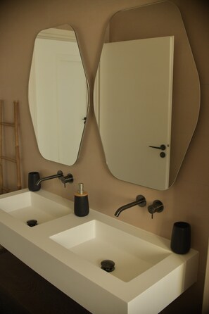A bathroom with a long white sink, two mirrors, and a door.