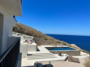 A modern outdoor pool area with a clear view of the ocean, stone steps leading to the pool, and lounge chairs.