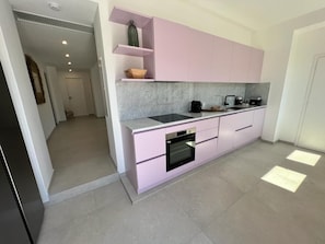A modern kitchen with pink cabinets, a black oven, and a marble countertop.