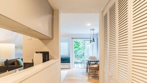 Ein Flur mit einer Couch, einem Tisch und Stühlen, der zu einem Balkon mit Blick auf Grün führt.