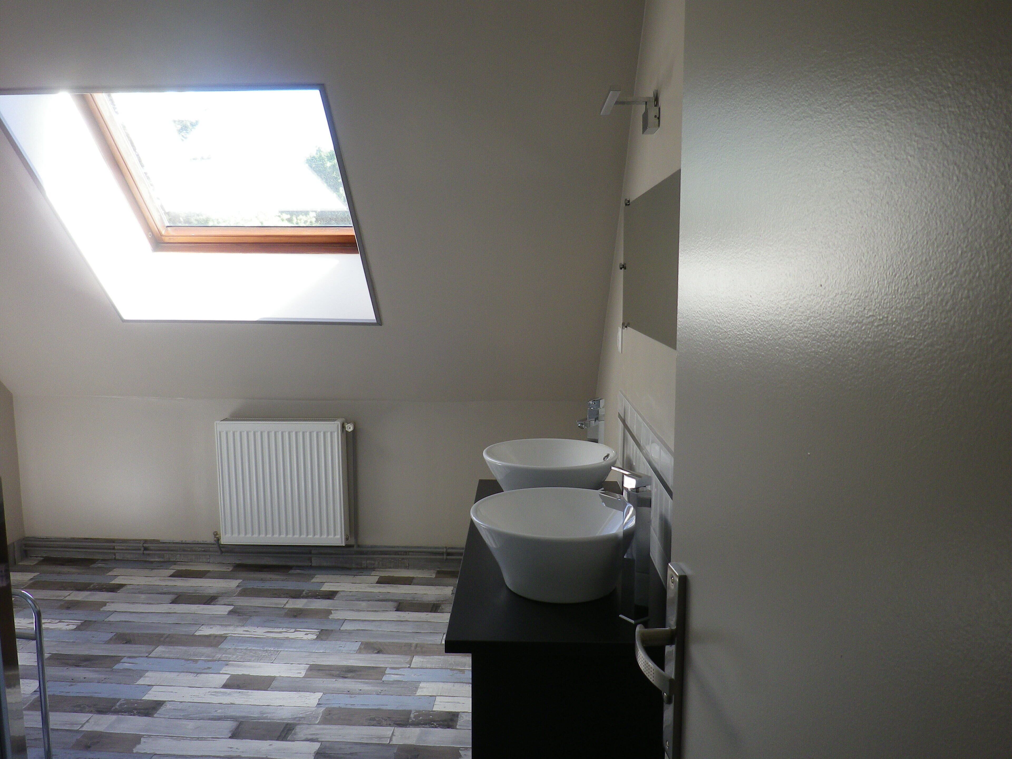 Une salle de bain avec un puits de lumière, deux lavabos, un radiateur et un sol carrelé.