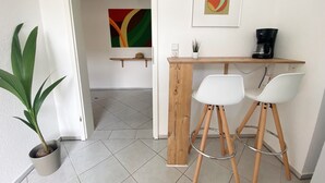 Angolo cottura con bancone in legno, due sedie bianche, una macchina da caffè e una pianta in vaso.