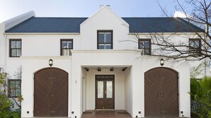 A two-story house with a symmetrical facade, featuring a central entrance with a double door and two side entrances with large wooden doors. - Winelands Golf Lodges 3 (Stellenbosch)