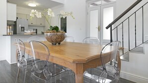 A dining area with a wooden table and clear chairs, a decorative bowl with flowers, and a staircase in the background. - Winelands Golf Lodges 3 (Stellenbosch)
