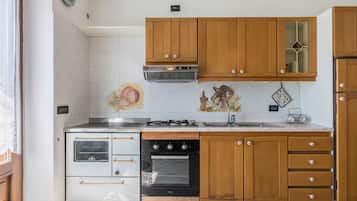 Een koelkast, een oven, een kookplaat, kookgerei, borden en bestek