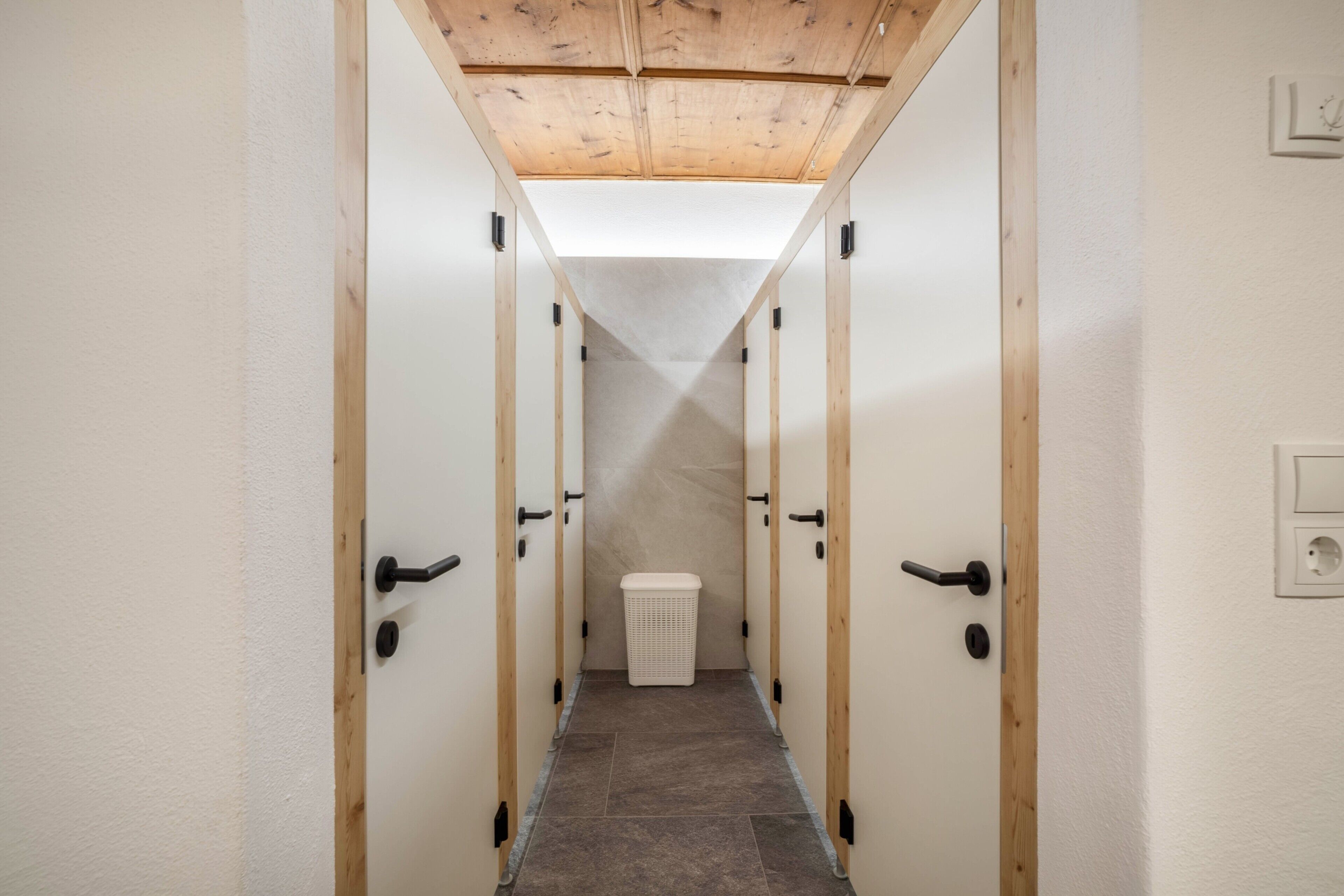 A narrow hallway with wooden doors and a white trash bin.