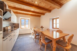 A modern kitchen with wooden beams, a dining area with a wooden table and chairs, and large windows. - 'Unterlanpacher Historic Refugium' with Mountain View, Garden & Terrace (Laces)