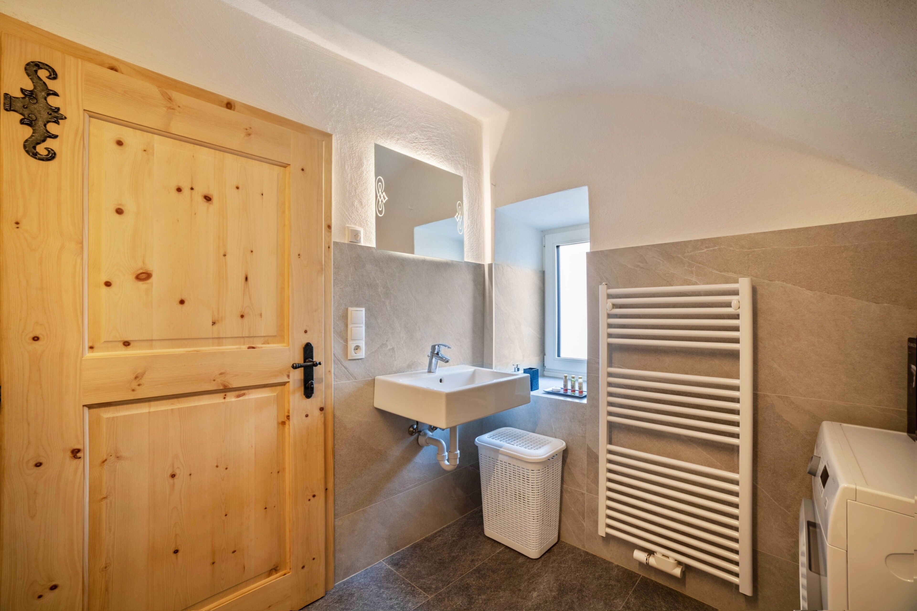 A bathroom with a wooden door, a white sink, a mirror, a towel rack, and a laundry basket.