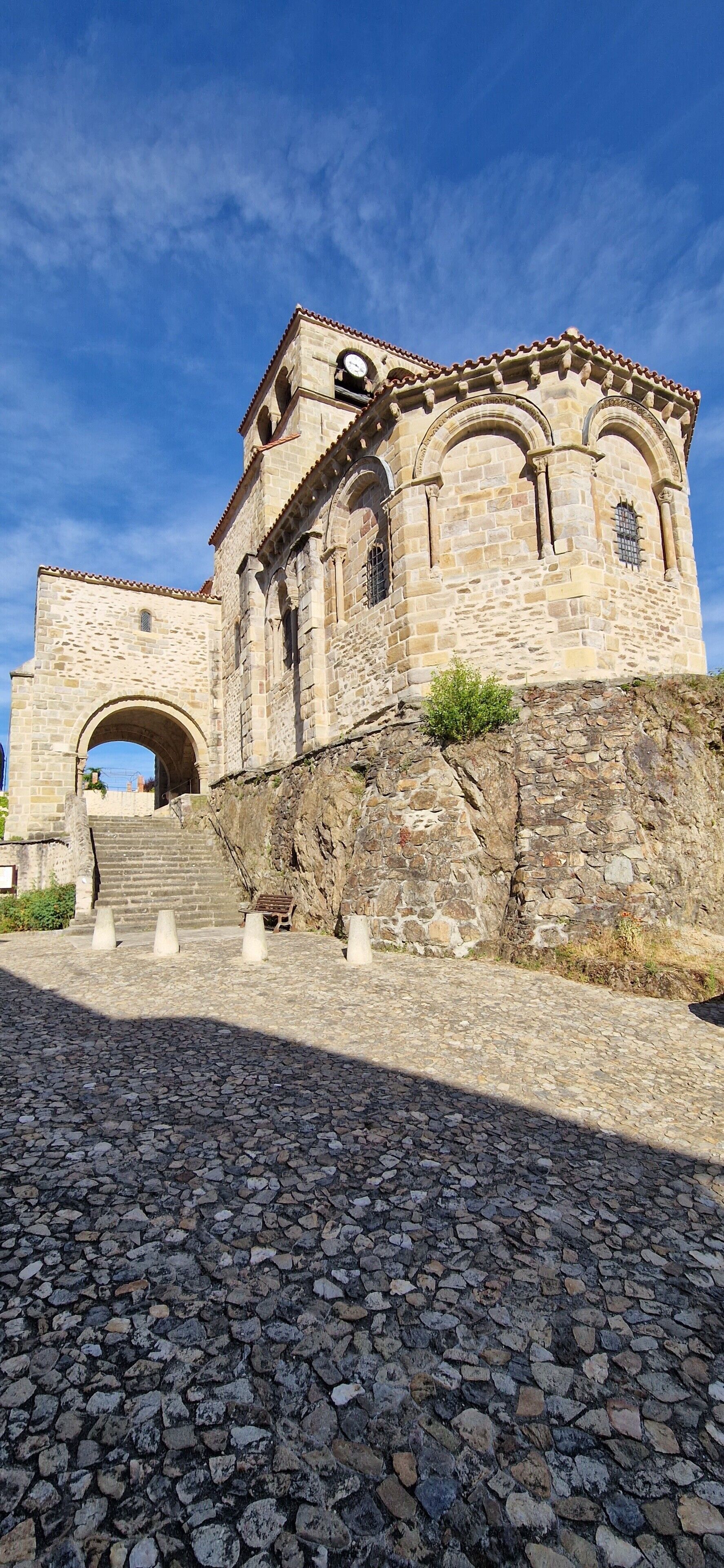Un edificio de piedra histórico con una entrada arqueada, una torre de reloj y una escalera que conduce a la entrada.