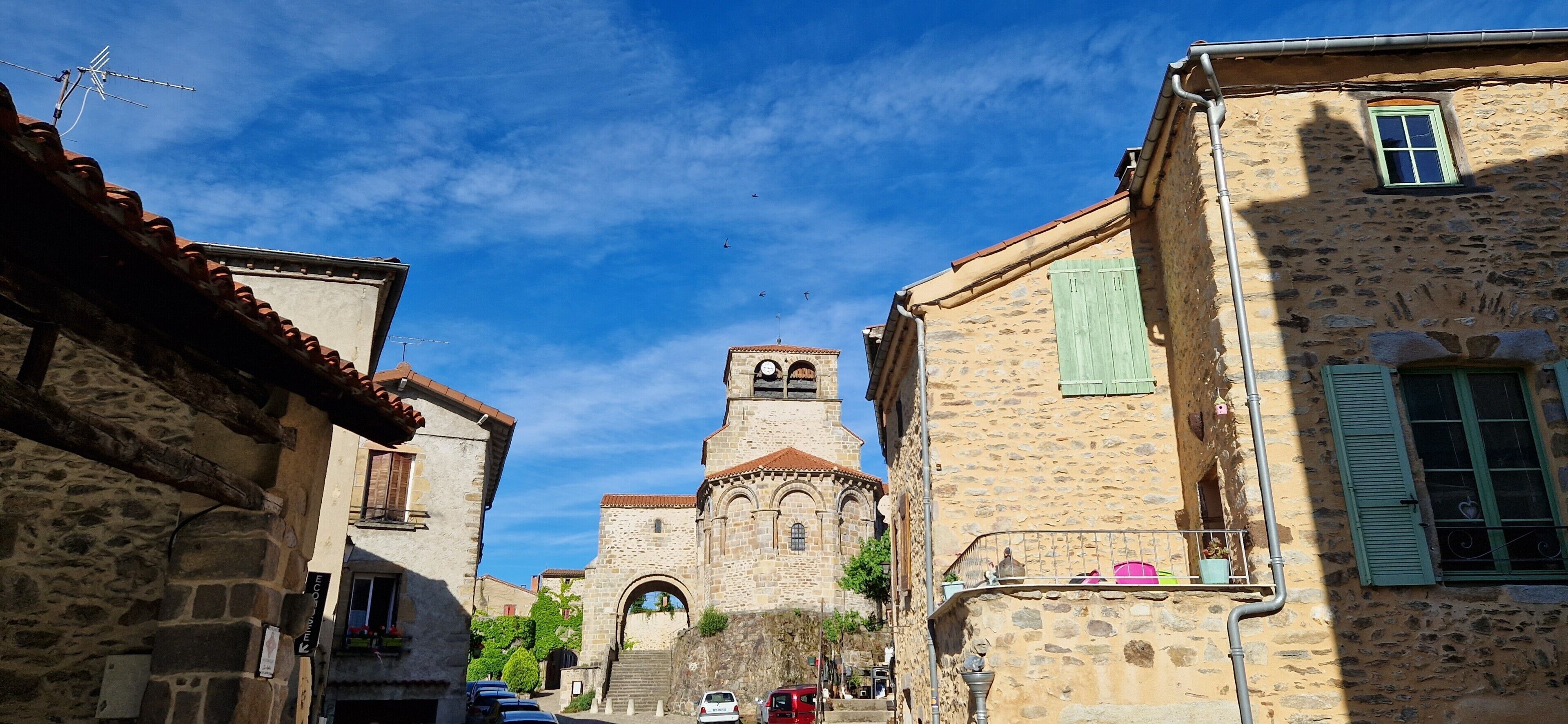 Une rue étroite bordée d’immeubles en pierre, une église dotée d’un clocher et un ciel d’un bleu limpide.
