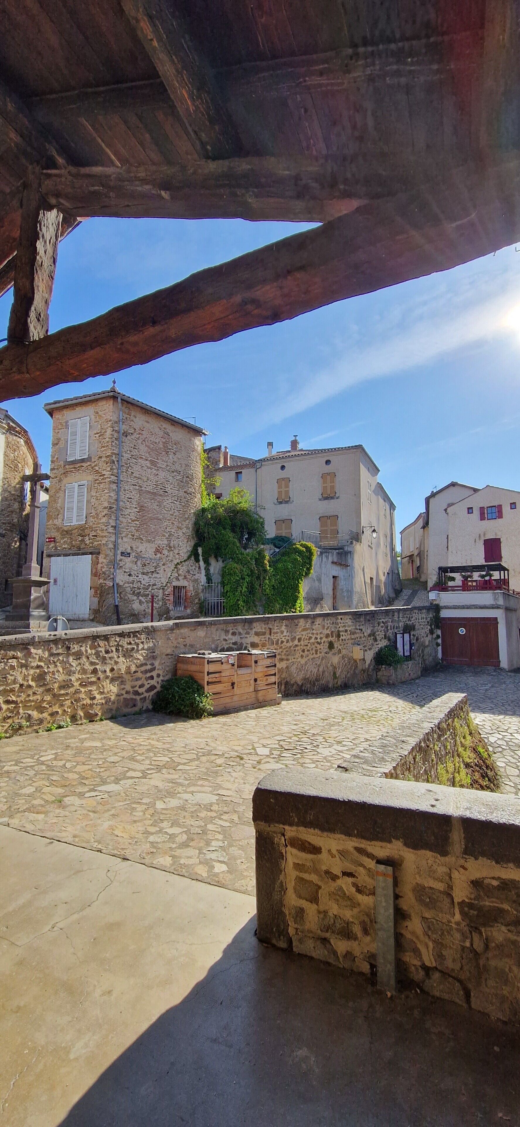 Une cour pavée de pierres, bordée de bâtiments, avec un banc en bois et un ciel dégagé.
