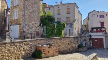 Une cour pavée de pierres, bordée de bâtiments, avec un banc en bois et un ciel dégagé.