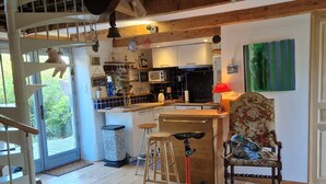 Une cuisine avec des poutres en bois, un coin repas avec une chaise, un tabouret de bar et un escalier.