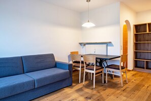 A modern living room with a sofa, dining table, chairs, a pendant light, and a bookshelf.