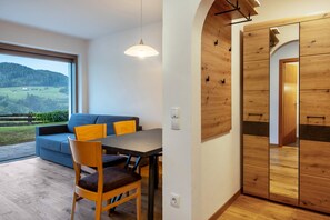 A modern interior with a dining area, wooden wardrobe, and a large window offering a view of the outdoors.