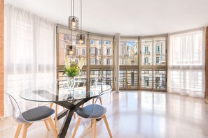Ein moderner Essbereich mit einem Glastisch, transparenten Stühlen und Blick auf eine Skyline durch große Fenster.