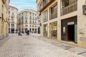 Una calle adoquinada flanqueada por edificios, con tiendas y una fuente en el centro.