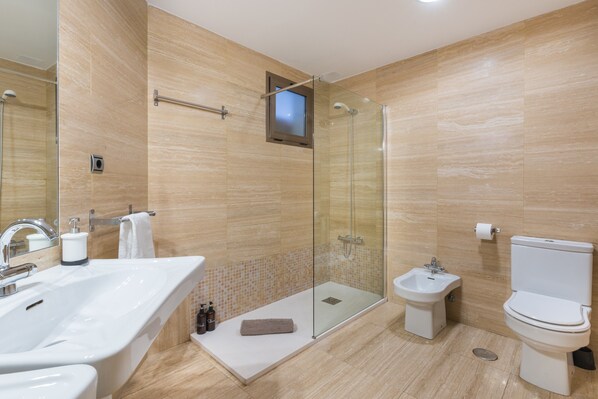 Un baño moderno con ducha envuelta en vidrio, una bañera amplia, un bidé y un inodoro.