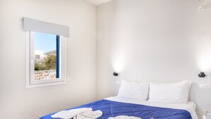 Ein Hotelzimmer mit Bett, weißen Wänden, einem Fenster mit Blick und einer blauen Bettdecke.