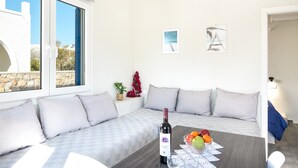 Ein modernes Wohnzimmer mit einer Couch, einem Esstisch mit einer Weinflasche und Obst, sowie zwei gerahmten Bildern an der Wand.