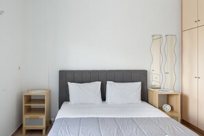 A bedroom with a bed, two pillows, a nightstand with a clock, and a wardrobe.