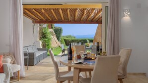 Ein Essbereich mit Tisch für zwei Personen, einem Korbsessel und Blick auf Garten und Berge.