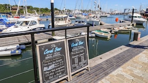 Un puerto deportivo con barcos amarrados, un cartel publicitario que anuncia 'The Coral Star' con detalles de reserva, y un cielo azul despejado.