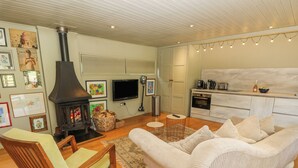 Una sala de estar acogedora con chimenea, un sofá, una silla de madera y una zona de cocina con cafetera.