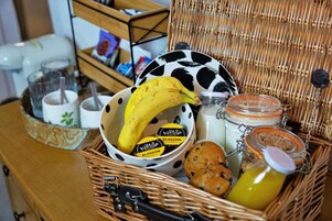 Una cesta de mimbre con una banana, galletas, un tarro de miel, una jarrón de leche y un frasco de vidrio con tapa.