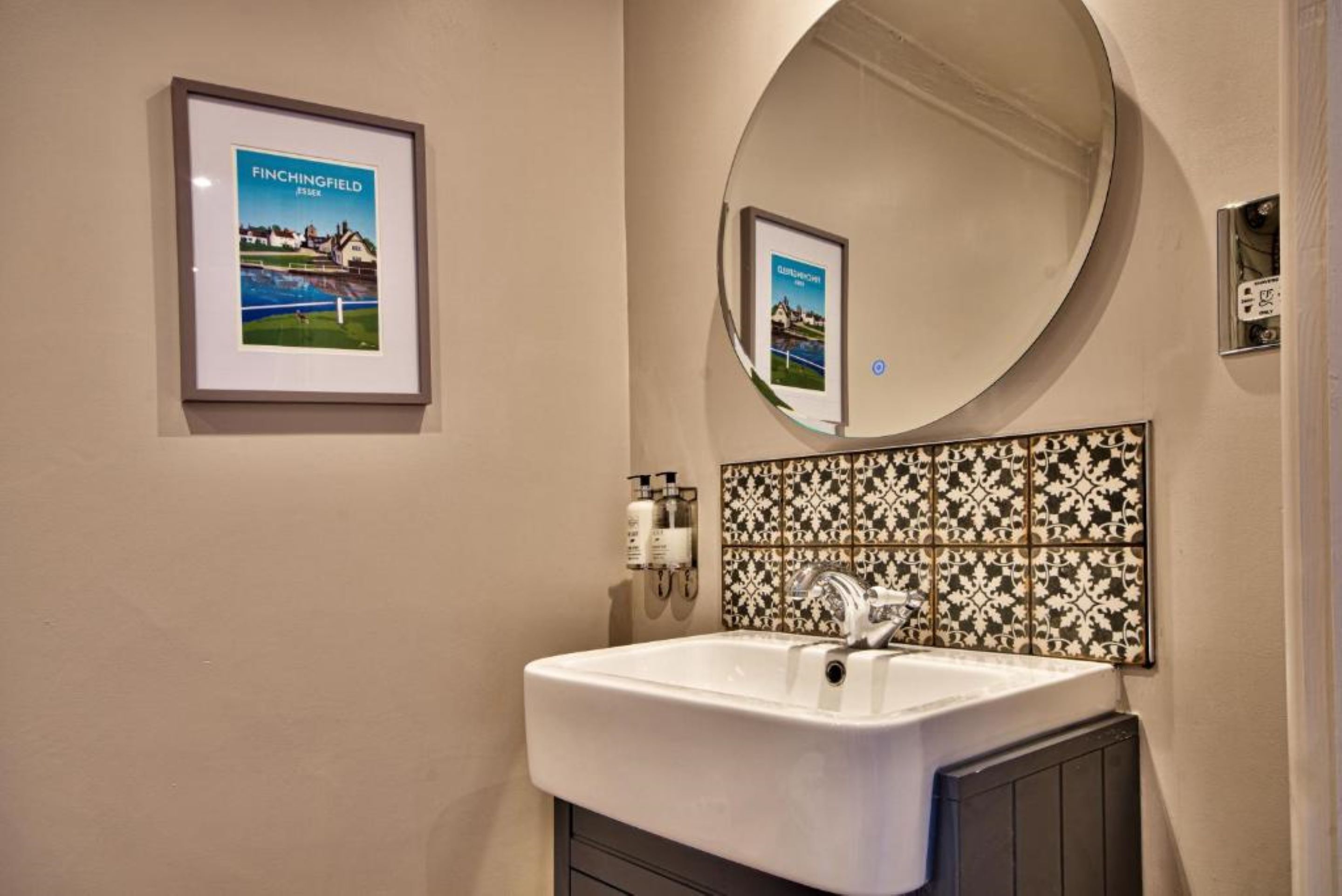 A bathroom with a white sink, a mirror, and a framed picture of a golf course.