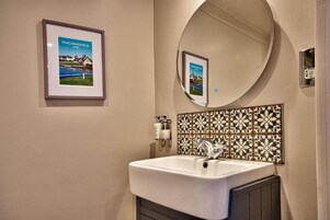 Un baño con lavamanos blanco, un espejo y un cuadro enmarcado de un campo de golf.