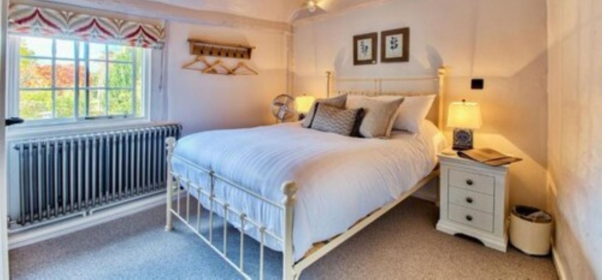 A bedroom with a single bed, a bedside table with a lamp, a radiator, and a window with curtains.